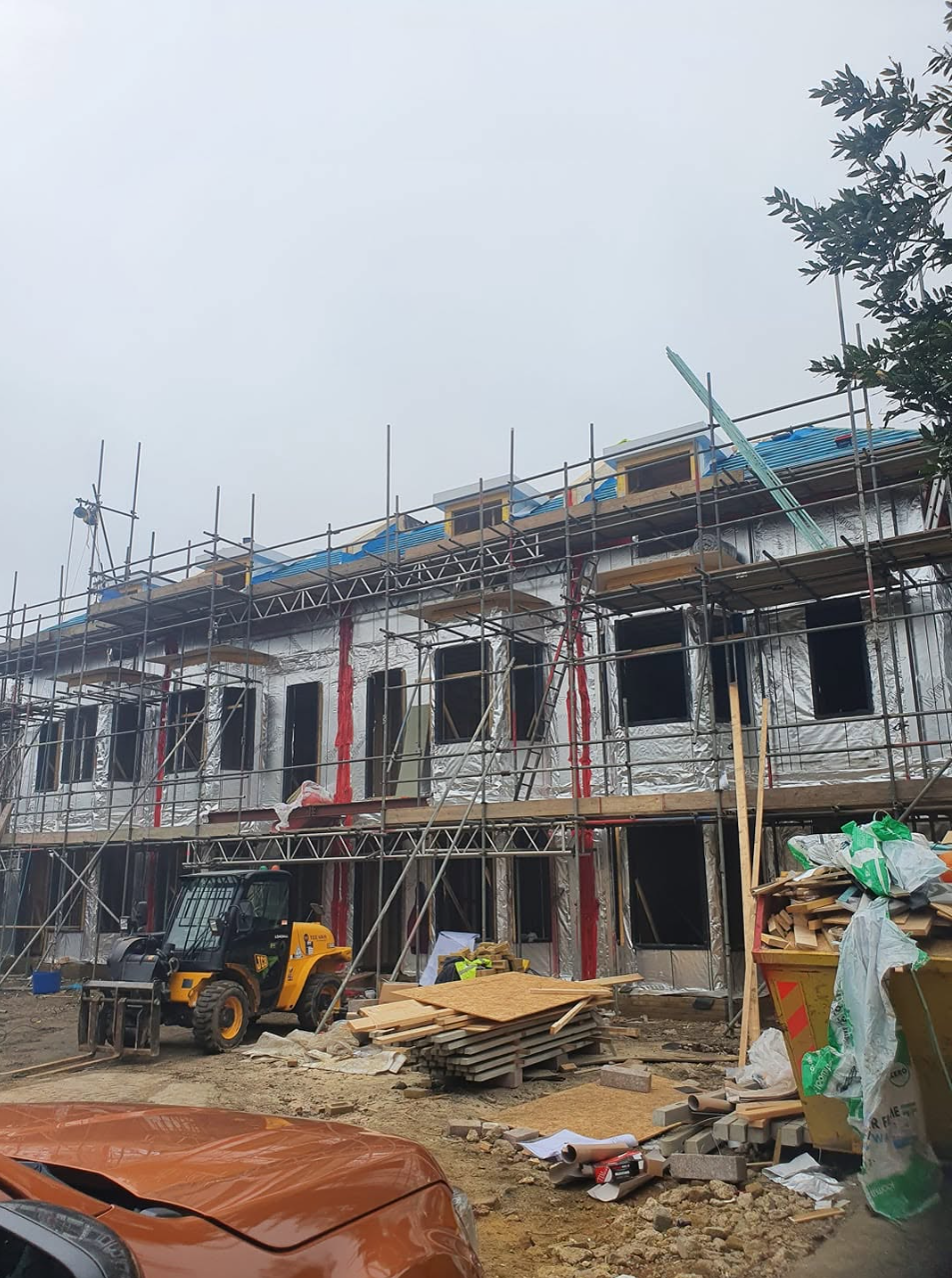 New-build terrace wrapped in breather membrane with full perimeter scaffold and telehandler on site