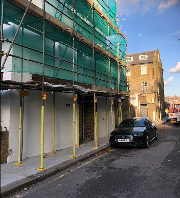 Terraced building with green-netted scaffold and cantilevered pavement fan protecting the footpath below