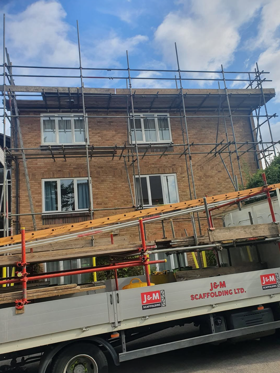 Two-storey brick semi with rear independent scaffold and J&M Scaffolding flatbed loaded with tube and boards