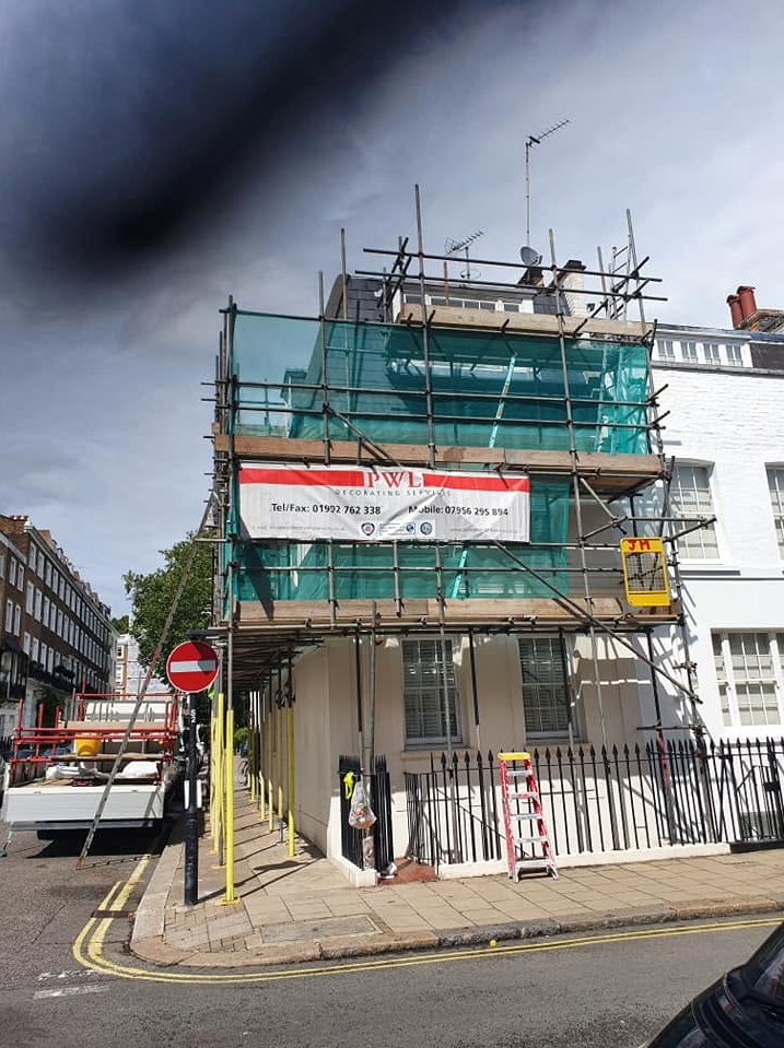 White stucco London townhouse with green-netted scaffold and pavement fan