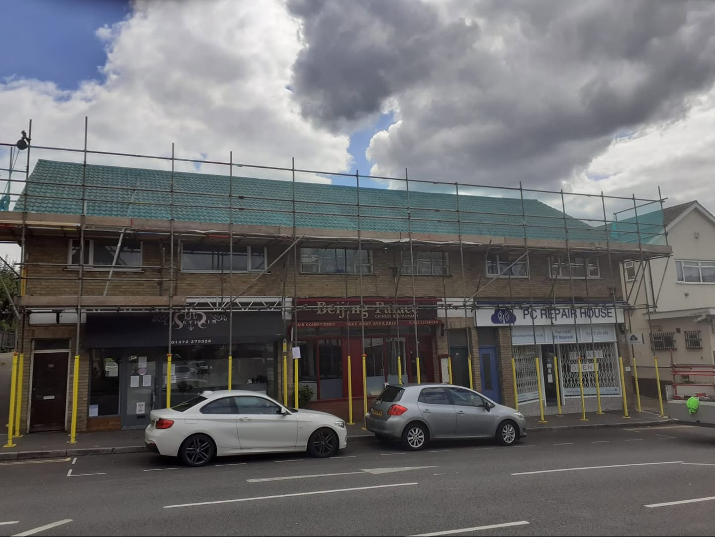 Retail parade with continuous roof-edge scaffold and yellow pedestrian protection standards over the shopfronts