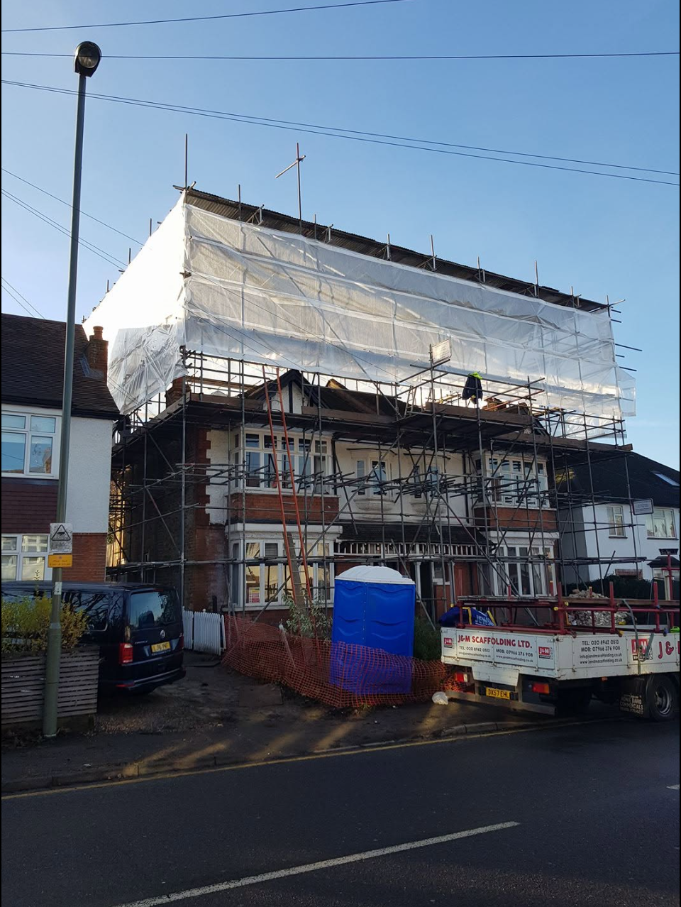 Semi-detached house with three-lift scaffold, temporary roof and shrink-wrap encapsulation, J&M Scaffolding truck parked outside