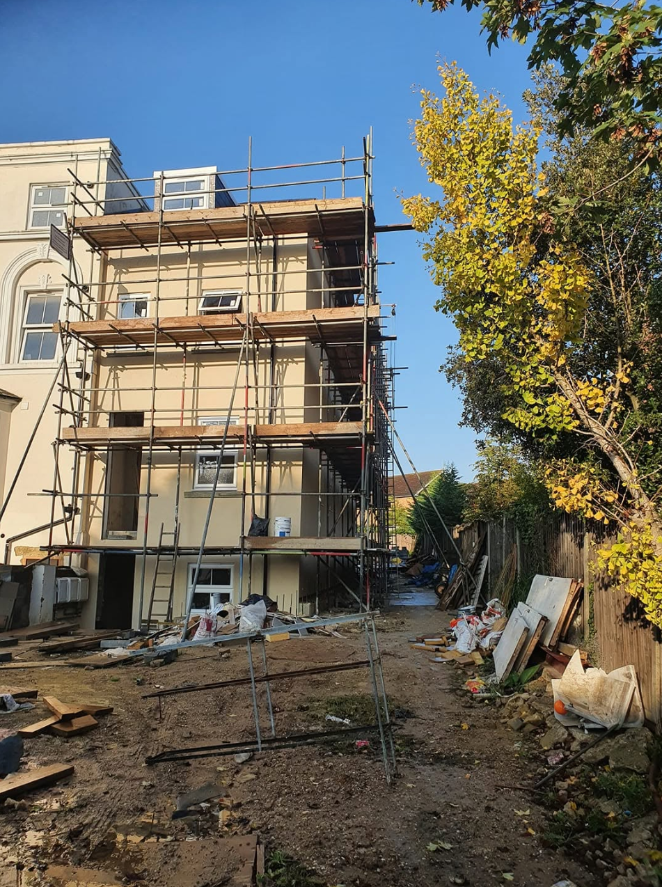 Four-lift rear scaffold on a rendered period property with ladder access and site works below